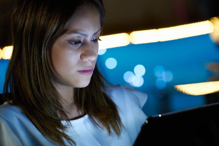 Young woman using a laptop at night with a thoughtful expression.