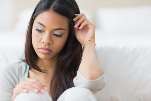 Young woman sitting on a bed looking at a pregnancy test with a worried expression.