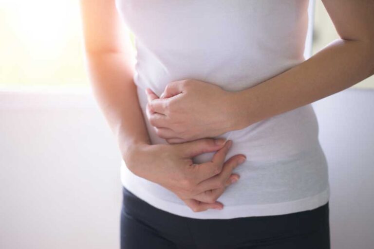 Woman standing indoors holding her stomach in discomfort.