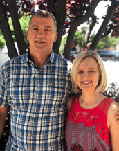 Portrait of a smiling man and woman standing together outdoors in front of a tree.