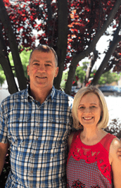 RealOptions Clinic - Education Staff. Portrait of a smiling man and woman standing together outdoors in front of a tree.