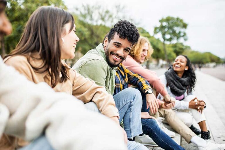Group of friends sitting outdoors on a walkway, talking and laughing together.