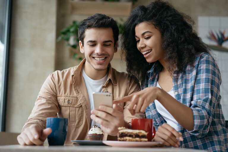 Smiling young couple sitting indoors looking at a phone together.