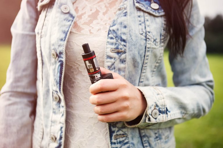Close-up of a person wearing a light wash denim jacket over a white lace top, holding device.