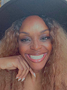 RealOptions Obria Medicical Clinic Staff. A close-up selfie of a smiling woman wearing a black hat and bright makeup, with long, wavy blonde and brown hair.