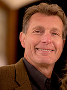 RealOptions Obria Medicical Clinic Staff. A headshot of a smiling middle-aged man with light brown hair, wearing a brown jacket over a dark shirt.