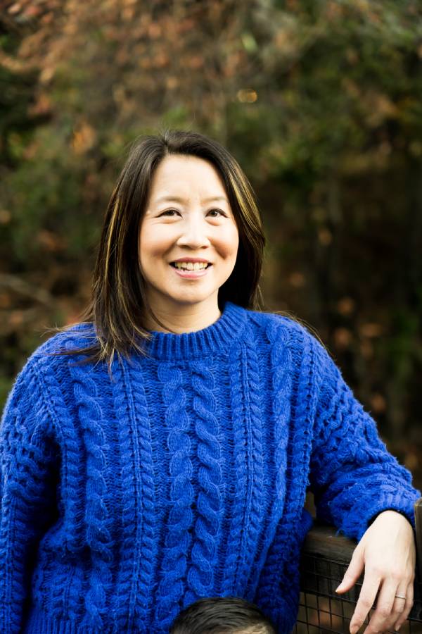 RealOptions Obria Medicical Clinic Staff. A smiling Asian woman with long dark hair, wearing a bright blue cable-knit sweater, posing outdoors in front of blurred trees.
