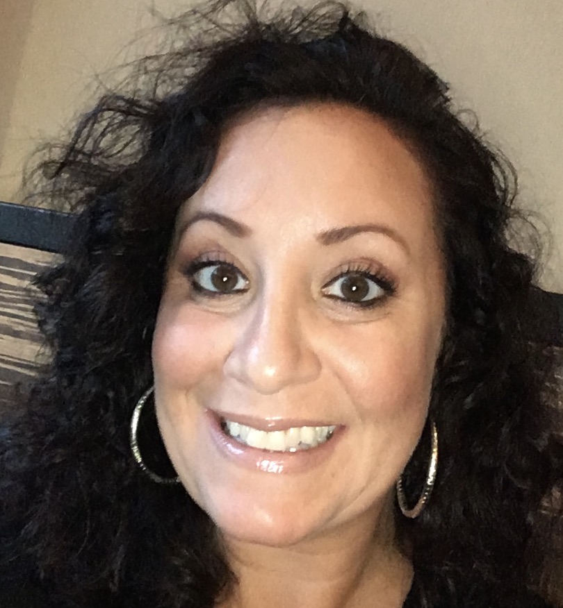 RealOptions Clinic - Education Staff. Close-up selfie of a smiling woman with long, dark, curly hair and large hoop earrings.