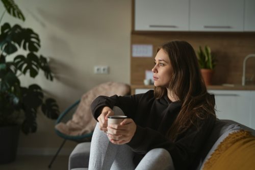 A woman sitting on a couch holding a mug contemplating her pregnancy options.